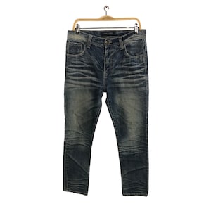 May include: Blue denim jeans with a faded wash and distressed details, hanging on a wooden hanger. The jeans have a classic five-pocket design and a button and zip closure. The background is white.