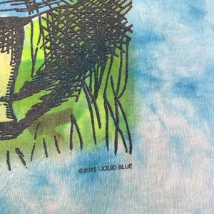 Peut inclure: Un t-shirt tie-dye avec un motif bleu et blanc semblable &agrave; un ciel. Le t-shirt pr&eacute;sente un motif graphique noir et vert. Le texte "&copy;2015 LIQUID BLUE" est imprim&eacute; au bas du t-shirt.