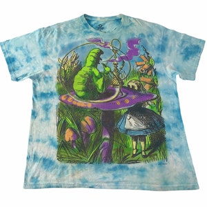Peut inclure: T-shirt bleu tie-dye avec un motif color&eacute; d'Alice au pays des merveilles. Le motif repr&eacute;sente une chenille verte fumant une chicha sur un champignon violet, avec Alice &agrave; proximit&eacute;. Le t-shirt a un col rond et des manches courtes.