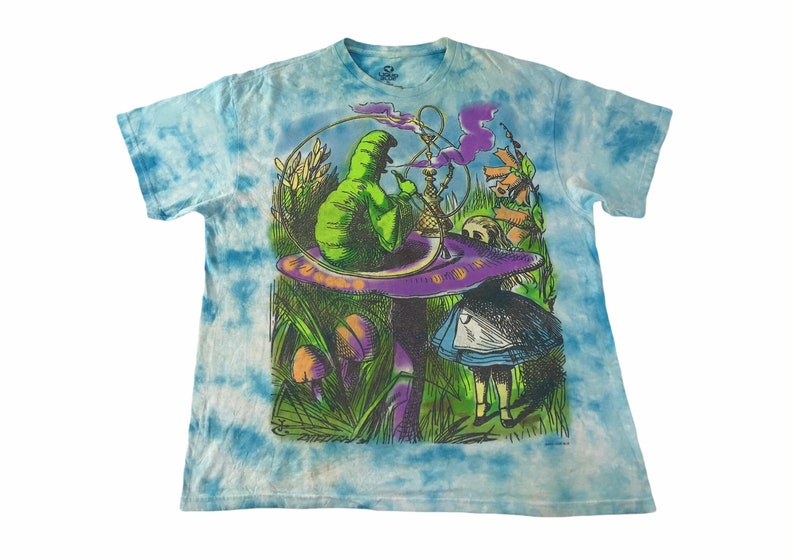 Peut inclure: T-shirt bleu tie-dye avec un motif color&eacute; d'Alice au pays des merveilles. Le motif repr&eacute;sente une chenille verte fumant une chicha sur un champignon violet, avec Alice &agrave; proximit&eacute;. Le t-shirt a un col rond et des manches courtes.