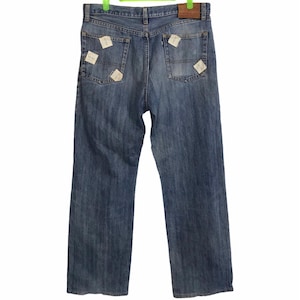 Könnte beinhalten: Hellblaue Jeans mit klassischem Fünf-Taschen-Design. Die Jeans haben einen geraden Bein-Schnitt und Patches auf den Gesäßtaschen. Ein brauner Lederaufnäher ist am Bund sichtbar. Die Jeans hängen an einem grünen Kleiderbügel.