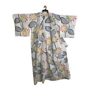May include: White Japanese kimono with a floral design. The kimono displays large, stylized flowers in yellow, pink, and red, alongside gray leaf shapes. The garment is suspended on a black hanger against a white backdrop.