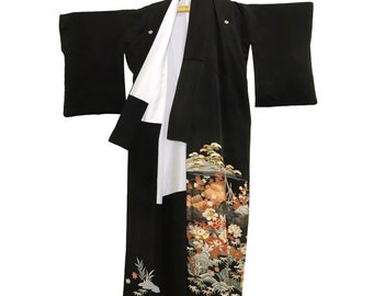 May include: A black kimono with white lining and a floral and landscape design. The kimono is hanging on a hanger, with the sleeves spread out. The design includes flowers, trees, and a mountain scene.