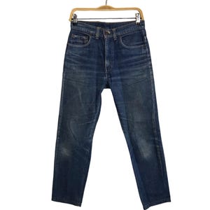 Könnte beinhalten: Eine blaue Jeans hängt an einem Holzbügel. Die Jeans hat ein klassisches Fünf-Taschen-Design, einen Knopf- und Reißverschluss und eine verwaschene Optik. Die Jeans ist im Straight-Leg-Stil.