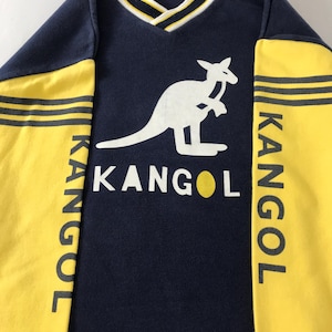 May include: Navy blue and yellow Kangol sweatshirt with a white kangaroo logo. The sleeves are yellow with black stripes and the word "KANGOL" printed vertically. The neckline is V-shaped with white and yellow trim.
