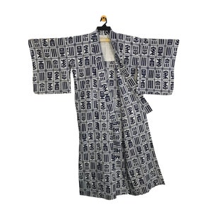 May include: A white and navy blue kimono with a repeating geometric pattern of Japanese characters and stripes. The garment is hanging on a wooden hanger, featuring long sleeves and a wrap-around design.
