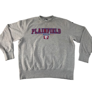 Pode incluir: Camisola cinzenta com a palavra "PLAINFIELD" em letras azuis e vermelhas no peito. Abaixo da palavra "PLAINFIELD" está a palavra "WRESTLING" em vermelho. Um pequeno emblema está centrado abaixo.