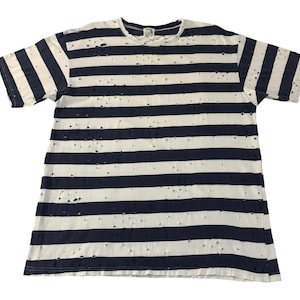 May include: White and navy blue striped t-shirt with a distressed design. The short-sleeved shirt features horizontal stripes and small holes throughout the fabric, giving it a vintage or worn look. The shirt is laid flat.