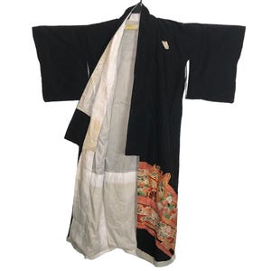 May include: A black kimono with wide sleeves, hanging open to reveal a white lining. The bottom edge features a colorful floral and geometric pattern in shades of red, orange, and green. The garment is displayed against a white background.