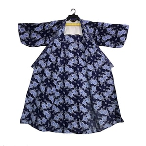 May include: A navy blue kimono with a floral pattern of light blue flowers and gray leaves. The kimono is open, revealing a white lining and is hanging on a black hanger. The sleeves are wide and the fabric appears to be lightweight.