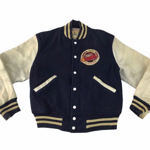 May include: A navy blue and cream varsity jacket with a patch on the chest. The jacket features cream-colored sleeves, a navy blue body, and a striped collar and cuffs. The patch has a red car graphic.