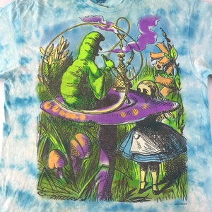 Peut inclure: T-shirt bleu clair tie-dye avec un motif color&eacute; d'Alice au pays des merveilles. Le motif repr&eacute;sente une chenille verte fumant une chicha sur un champignon, avec Alice. Le t-shirt porte une &eacute;tiquette Liquid Blue.