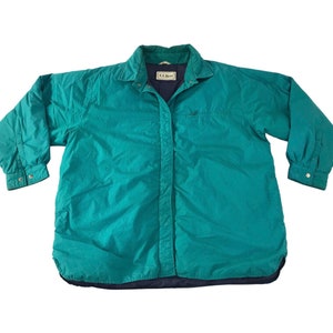 May include: Teal quilted jacket with a button-down front and collared neckline. The jacket has long sleeves with buttoned cuffs and a navy blue lining. The label reads "L.L. Bean".