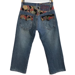 May include: Blue denim jeans with a patchwork design on the back pockets. The patches are made of colourful fabric with floral and geometric patterns.
