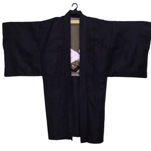 May include: A dark navy blue kimono hangs from a black hanger. The traditional Japanese garment features wide sleeves and a long, open front. The interior lining is visible, showcasing a patterned design with shades of white, pink, and brown.