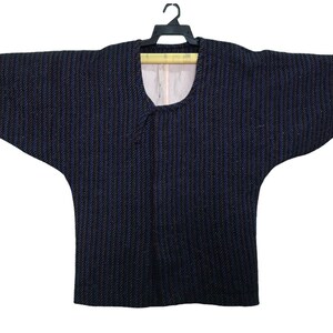 May include: A dark blue kimono-style jacket with a vertical striped pattern. The jacket has wide sleeves and a V-neck collar. It is hanging on a black hanger against a white background. The interior lining is a light beige colour.