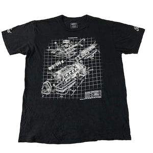 Peut inclure: T-shirt noir avec un schéma blanc d'un moteur Ford. Le schéma montre les composants du moteur sur un fond quadrillé. Le logo Ford est visible en bas. Le t-shirt a des manches courtes.