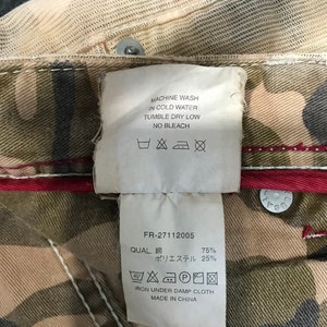 May include: A white tag with black text and care instructions for a garment. The tag says "Machine wash in cold water, tumble dry low, no bleach".  The tag also includes a size 40 symbol and a symbol for ironing under a damp cloth. The tag also says "FR-27112005, QUAL. 綿 75%, ポリエステル 25%, IRON UNDER DAMP CLOTH, MADE IN CHINA".