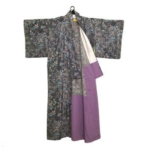 Può includere: Un kimono grigio scuro con un motivo floreale blu, arancione e bianco. Il kimono ha una fodera bianca e un pannello viola all'interno. È appeso a una gruccia nera.