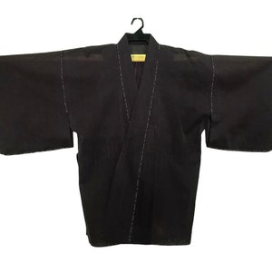 May include: A black kimono-style robe with wide sleeves, hanging on a black hanger. The robe has a V-neck and is accented with white stitching along the seams. The garment is made of a dark fabric.