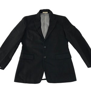 Puede incluir: Un blazer negro con cierre de dos botones, dos bolsillos delanteros y solapa con muescas. El forro interior es de color gris claro. Las mangas tienen botones en los pu&ntilde;os. El blazer se muestra sobre un fondo blanco.