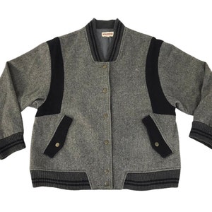 May include: Gray wool bomber jacket with black accents on the shoulders, pockets, and cuffs. The jacket has a button-up front and a ribbed collar and cuffs. The brand name is visible on the collar.