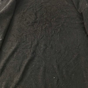 K&ouml;nnte beinhalten: Schwarzer Kapuzenpullover mit strukturiertem Stoff und einem wei&szlig;en Etikett am Ausschnitt. Das Innere des Sweatshirts ist sichtbar und zeigt das weiche, dunkle Material. Der Stoff hat kleine, helle Flecken.