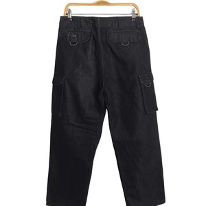 May include: Black denim cargo trousers hanging on a wooden hanger. The trousers feature two back pockets with metal hardware and two side cargo pockets. The dark wash trousers have a relaxed fit.
