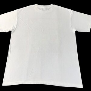 May include: A plain white t-shirt, viewed from the back, against a black background. The short-sleeved shirt is made of a soft material and has a crew neck. The fabric has subtle wrinkles.