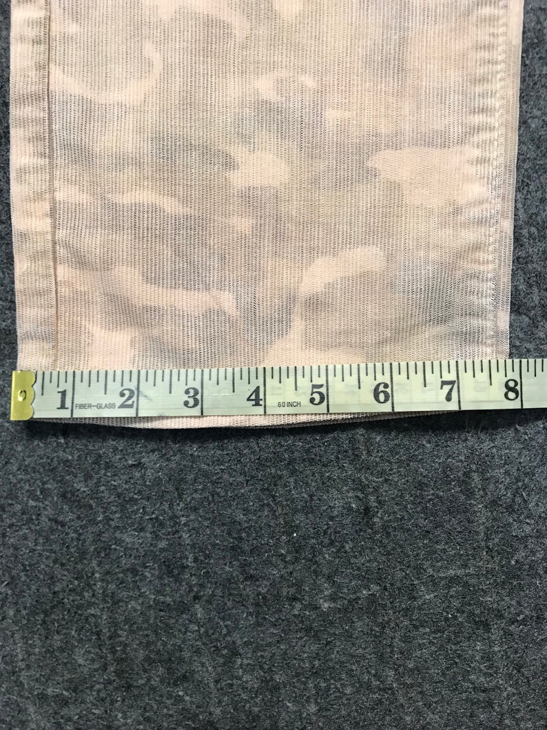 May include: A close-up of a beige fabric with a camouflage pattern. A measuring tape is placed on the fabric, showing measurements from 1 to 8 inches.