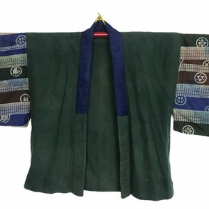 May include: A dark green kimono jacket with a navy blue collar and sleeve details. The sleeves have a patchwork design with geometric and circular patterns in blue, brown, and white. The jacket is displayed against a white backdrop.