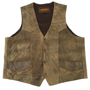 Peut inclure: Un gilet en daim marron avec une fermeture boutonnée et deux poches avant. Le gilet a un col en V et une doublure intérieure marron foncé. Le gilet porte une étiquette avec le mot "UNIK" en or.