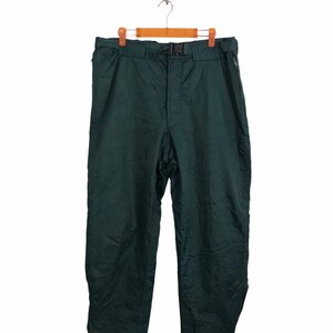 May include: Dark green trousers with a belt and buckle closure, hanging on a wooden hanger. The trousers have a straight leg design and a side zip. The fabric has a slightly wrinkled texture.