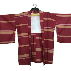 May include: A burgundy kimono with horizontal tan and light pink stripes. The traditional Japanese garment is displayed open, revealing a white interior. The sleeves are wide and the fabric appears to be lightweight.
