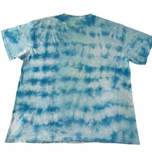 Peut inclure: Un t-shirt tie-dye bleu clair et blanc. Le t-shirt a un col rond et des manches courtes. Le motif tie-dye se compose de bandes horizontales bleues et blanches, cr&eacute;ant un effet ray&eacute;. Le t-shirt est en tissu doux et l&eacute;ger.