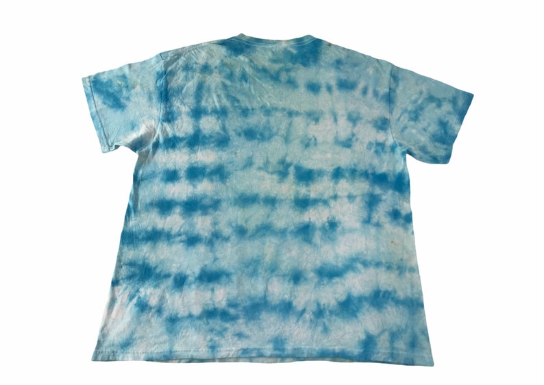 Peut inclure: Un t-shirt tie-dye bleu clair et blanc. Le t-shirt a un col rond et des manches courtes. Le motif tie-dye se compose de bandes horizontales bleues et blanches, cr&eacute;ant un effet ray&eacute;. Le t-shirt est en tissu doux et l&eacute;ger.