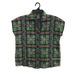 May include: A short-sleeved shirt with a black background and a repeating pattern of green, yellow, and blue floral designs. The shirt is button-down with a collar and is hanging on a black hanger.