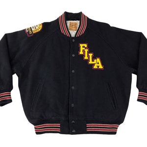 May include: Black varsity jacket with the word "FILA" in yellow letters. The jacket has a red, white, and black striped trim on the cuffs, collar, and waist. A patch is visible on the upper left sleeve.