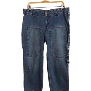 May include: Blue denim jeans with a studded belt and multiple pockets. The jeans have a relaxed fit and a straight leg.