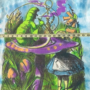 Peut inclure: Un t-shirt tie-dye avec un graphisme color&eacute; d'Alice au pays des merveilles. Le motif repr&eacute;sente une chenille verte fumant une pipe &agrave; eau sur un champignon violet, avec Alice en arri&egrave;re-plan. Le t-shirt mesure environ 63,5 cm de large.