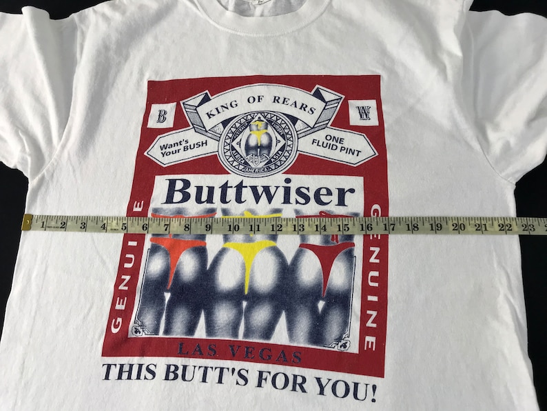 May include: White t-shirt with a graphic parody of a beer label, featuring the word "Buttwiser" and images of three posteriors in colorful underwear. The text includes "King of Rears" and "This Butt's For You!"