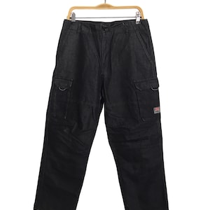 May include: Black denim cargo trousers with multiple pockets and a relaxed fit. The trousers are hanging on a wooden hanger against a white background. Features include two large side pockets and a small logo patch.