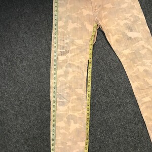 May include: A pair of light brown camouflage print jeans with a brown leather patch that says "FLAM REPORT" on the back waistband.