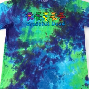 Puede incluir: Una camiseta tie-dye con un patr&oacute;n de remolino azul, verde y morado. La camiseta presenta un gr&aacute;fico de osos bailando y el texto "Grateful Dead" en blanco.