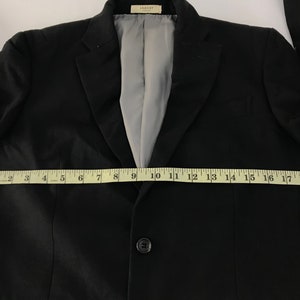Puede incluir: Un blazer negro con cierre de un solo bot&oacute;n, solapa con muescas y forro interior gris. El blazer se mide con una cinta m&eacute;trica amarilla, que muestra un ancho de aproximadamente 50 cm.