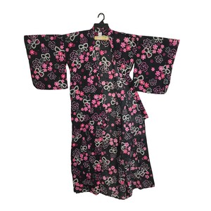 May include: Black kimono with a floral pattern of pink flowers and white bows. The kimono is hanging on a black hanger. The sleeves are wide and the garment is open at the front.