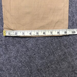 Pu&ograve; includere: Tessuto beige con motivo a griglia misurato con un metro a nastro. Il metro a nastro mostra una lunghezza di circa 25 cm. Il tessuto &egrave; su una superficie grigia.