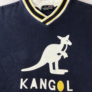 May include: Navy blue V-neck sweatshirt featuring a white kangaroo logo and the brand name "KANGOL" in white block letters. The collar has a white base with yellow and navy blue stripes. The brand's logo is visible on the collar.