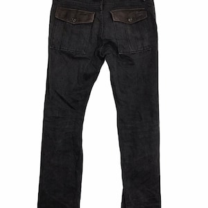 Puede incluir: Pantalones vaqueros grises oscuros con dos bolsillos traseros con detalles de ante marrón. Los pantalones tienen un diseño clásico de cinco bolsillos y un corte de pierna recta. Los bolsillos traseros tienen cierres de botón.