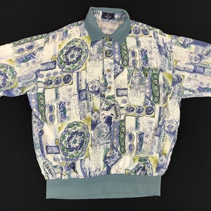 May include: Short-sleeved shirt with a unique pattern in white, blue, and green. The shirt features a teal collar and a matching elastic waistband. The design includes abstract shapes and floral motifs.